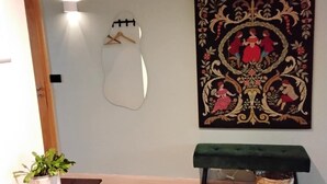 Una habitación con piso de madera, un banco verde, una lámpara de pared, una planta en maceta y un tapiz decorativo grande.
