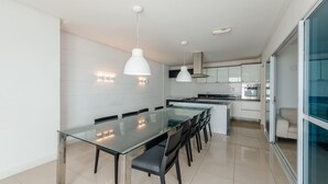 Een moderne keuken met een glazen eettafel, hanglampen en uitzicht op de woonkamer.