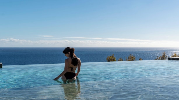 Une personne se trouve dans une piscine à débordement dont l’eau est cristalline, et qui offre une vue sur l’océan.