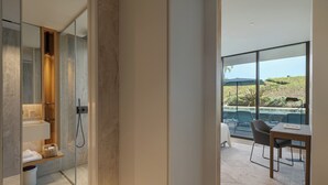 Une salle de bain moderne dotée d’une douche à parois de verre, d’un meuble-lavabo en bois et offrant une vue sur une piscine et un espace de détente extérieur.
