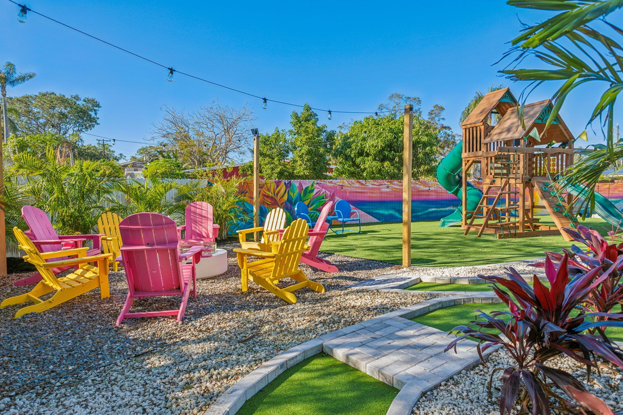 A playground with slides and climbing structures, surrounded by gravel and greenery.