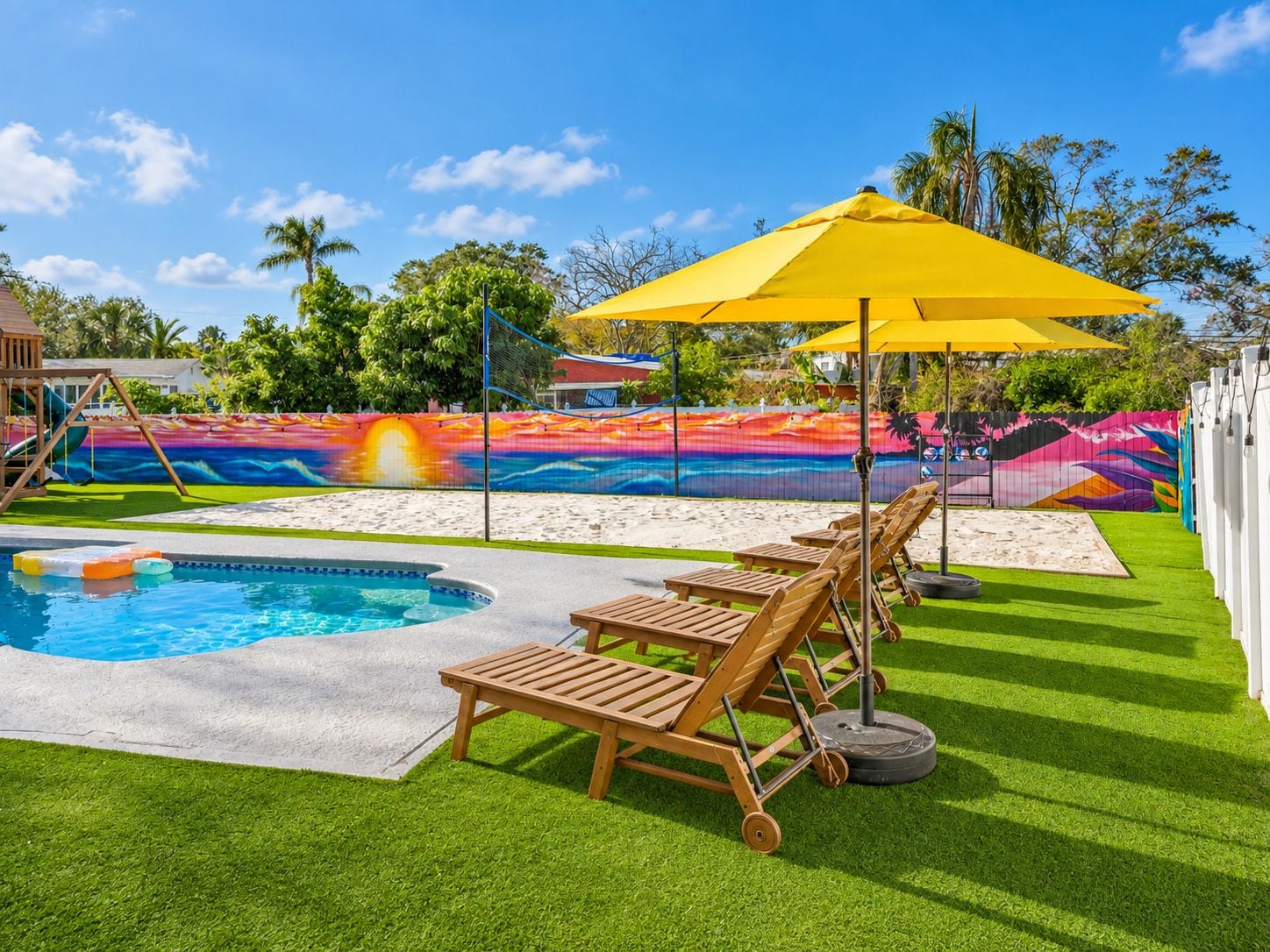 A swimming pool with a colorful mural, a sun chair, and a yellow umbrella.