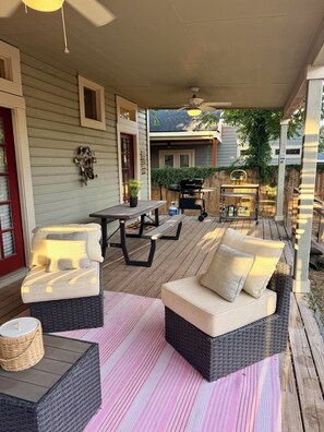 A covered patio with wicker furniture, a picnic table, and a ceiling fan.