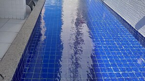 A swimming pool with blue tiles, surrounded by white tiled walls and a concrete edge.