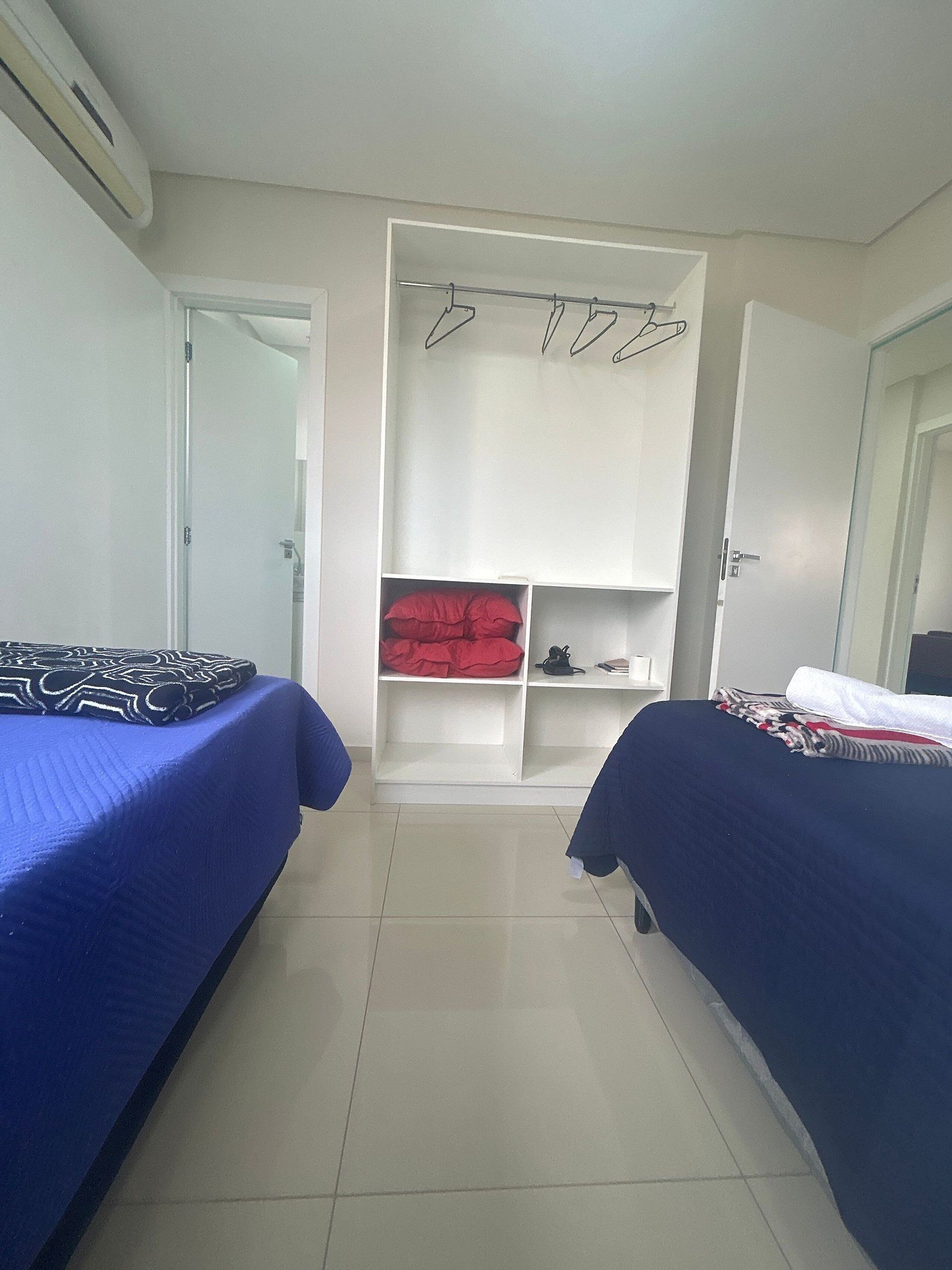 Une chambre avec deux lits, une armoire avec espace pour suspendre les vêtements et un sol carrelé.
