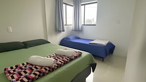 Une chambre avec un grand lit, un plus petit lit et une fenêtre avec des rideaux.