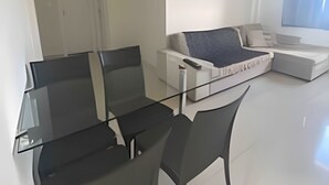 Un salon moderne avec une table à manger en verre, des chaises noires, un canapé blanc et une fenêtre avec des rideaux.