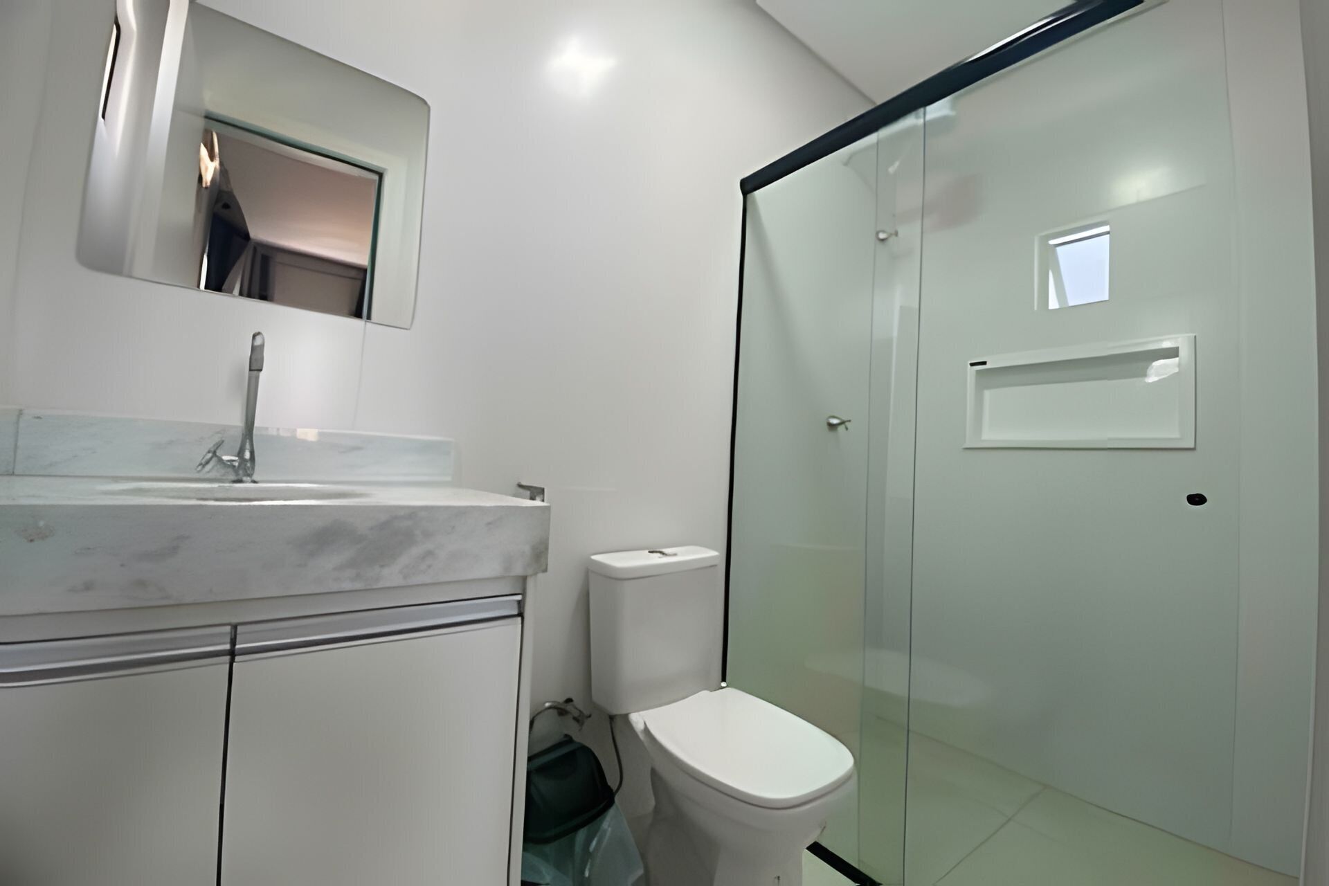 A modern bathroom with a marble sink, a toilet, and a glass shower enclosure.