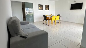 A modern living room with a grey sofa, a dining table with yellow chairs, a flat-screen TV mounted on the wall, and a balcony door. - Close to the waterfront, 14 people, air conditioning and garage (Petrolina)