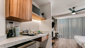 A compact kitchen with a built-in dishwasher, a coffee maker, and a blender. There is a wooden cabinet above the counter and a ceiling fan above. - Suites Álamos by Homirent (Querétaro)