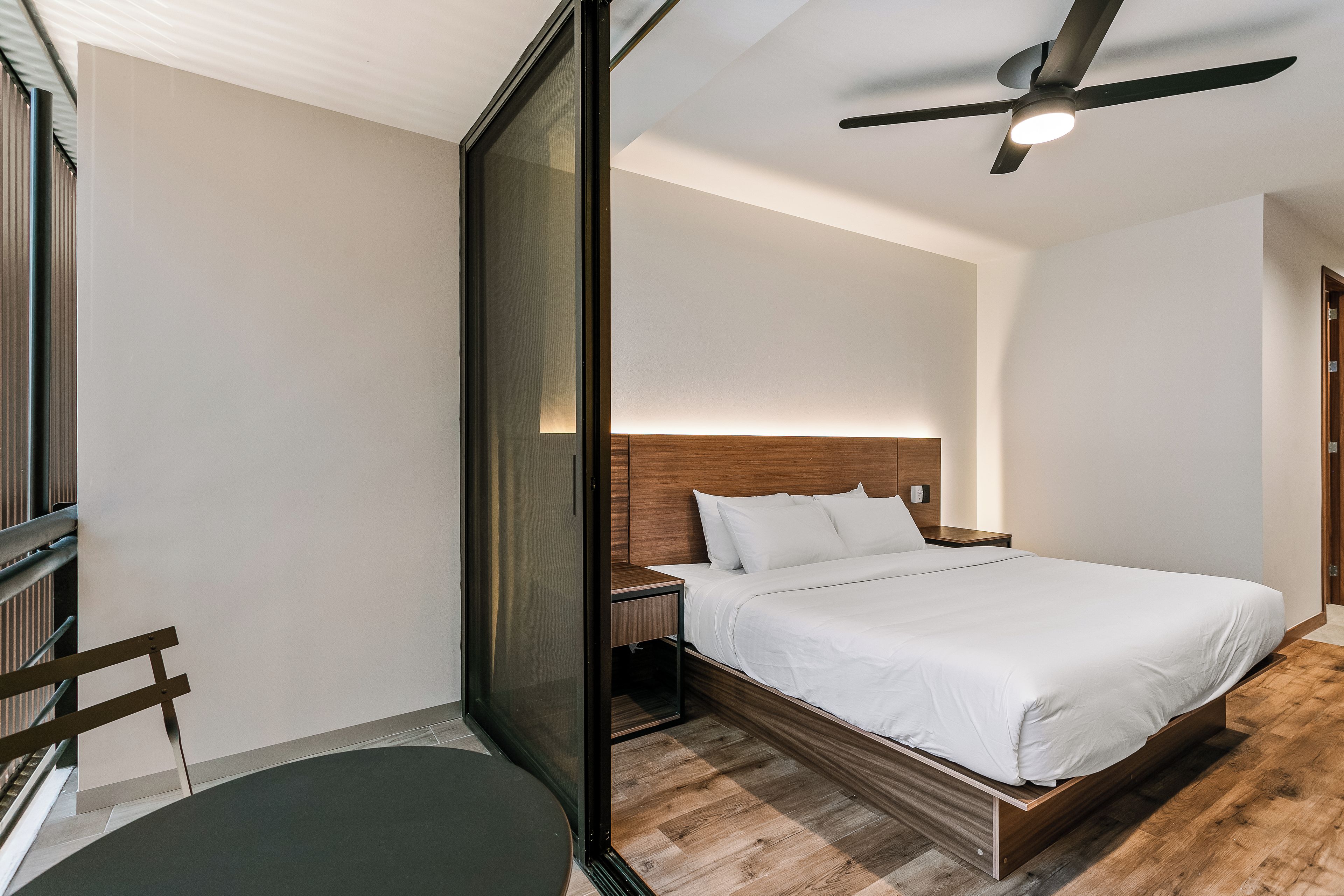 A modern hotel room with a large bed, a ceiling fan, and a view of the outdoors.