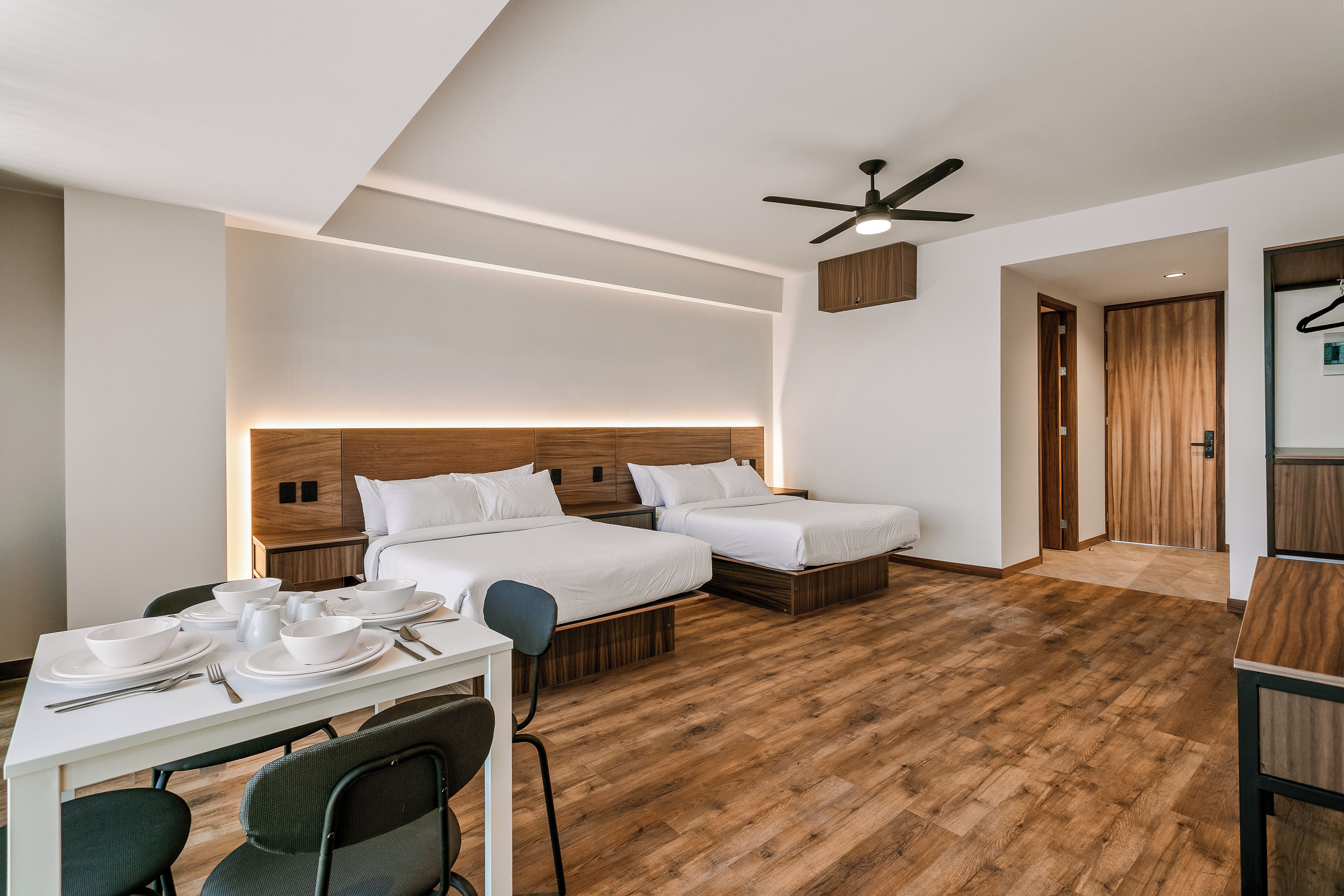 Ein Hotelzimmer mit Holzboden, zwei Betten, einem Esstisch mit Stühlen und einem Deckenventilator.