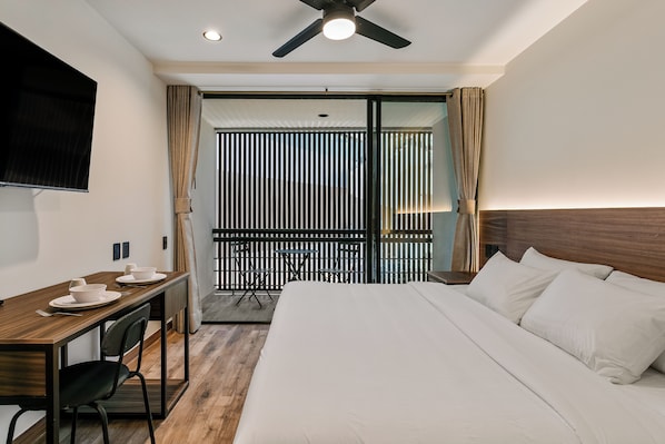 A hotel room with a bed, a desk with a chair, a TV, and a balcony with a view.