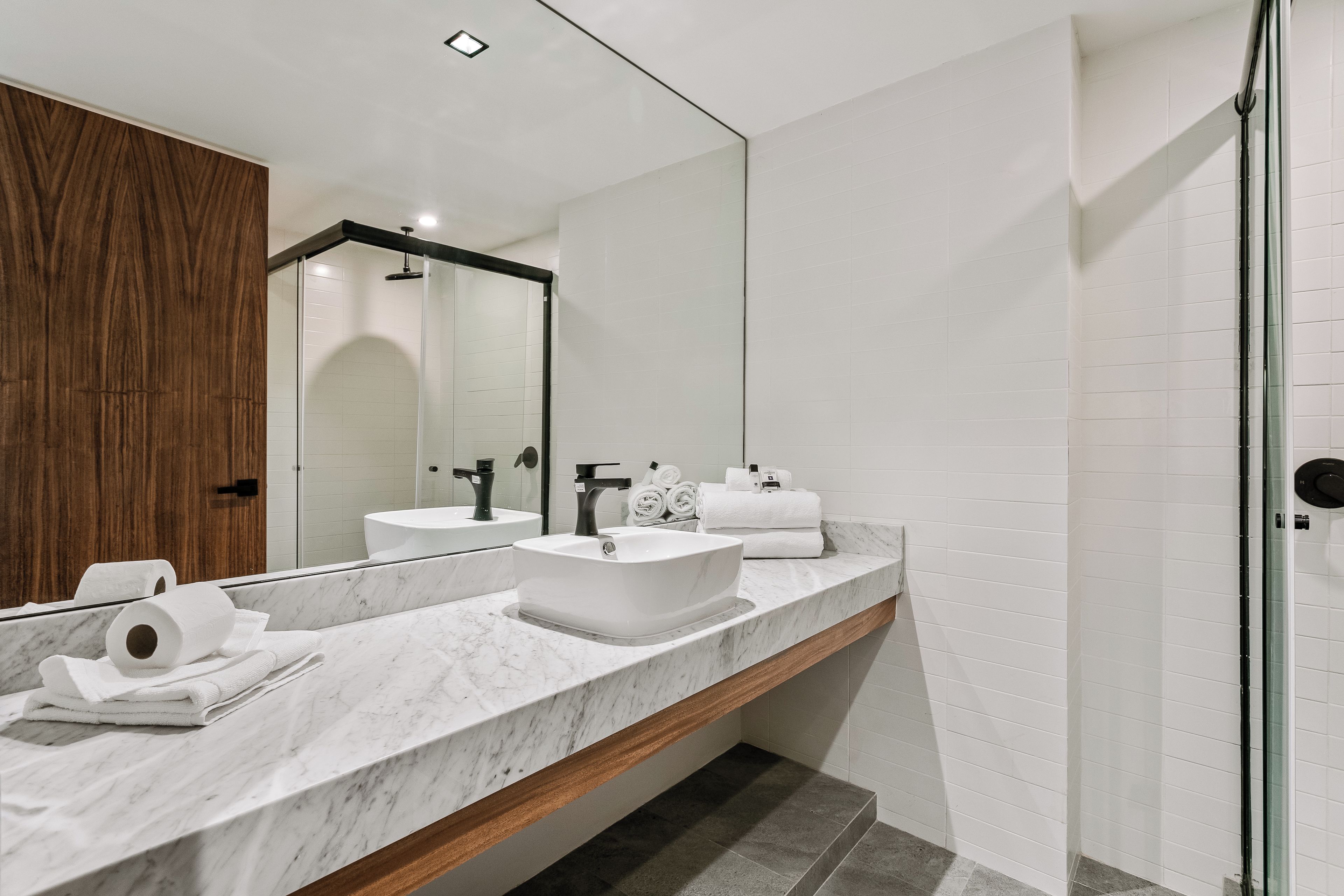 Ein modernes Badezimmer mit Marmorplatte, zwei Waschbecken, einem großen Spiegel und einer Duschkabine aus Glas.