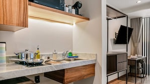 A compact kitchen with a built-in microwave, a sink, and a stove. There is a small dining area with a table and chairs, and a separate space with a TV and curtains. - Suites Álamos by Homirent (Querétaro)