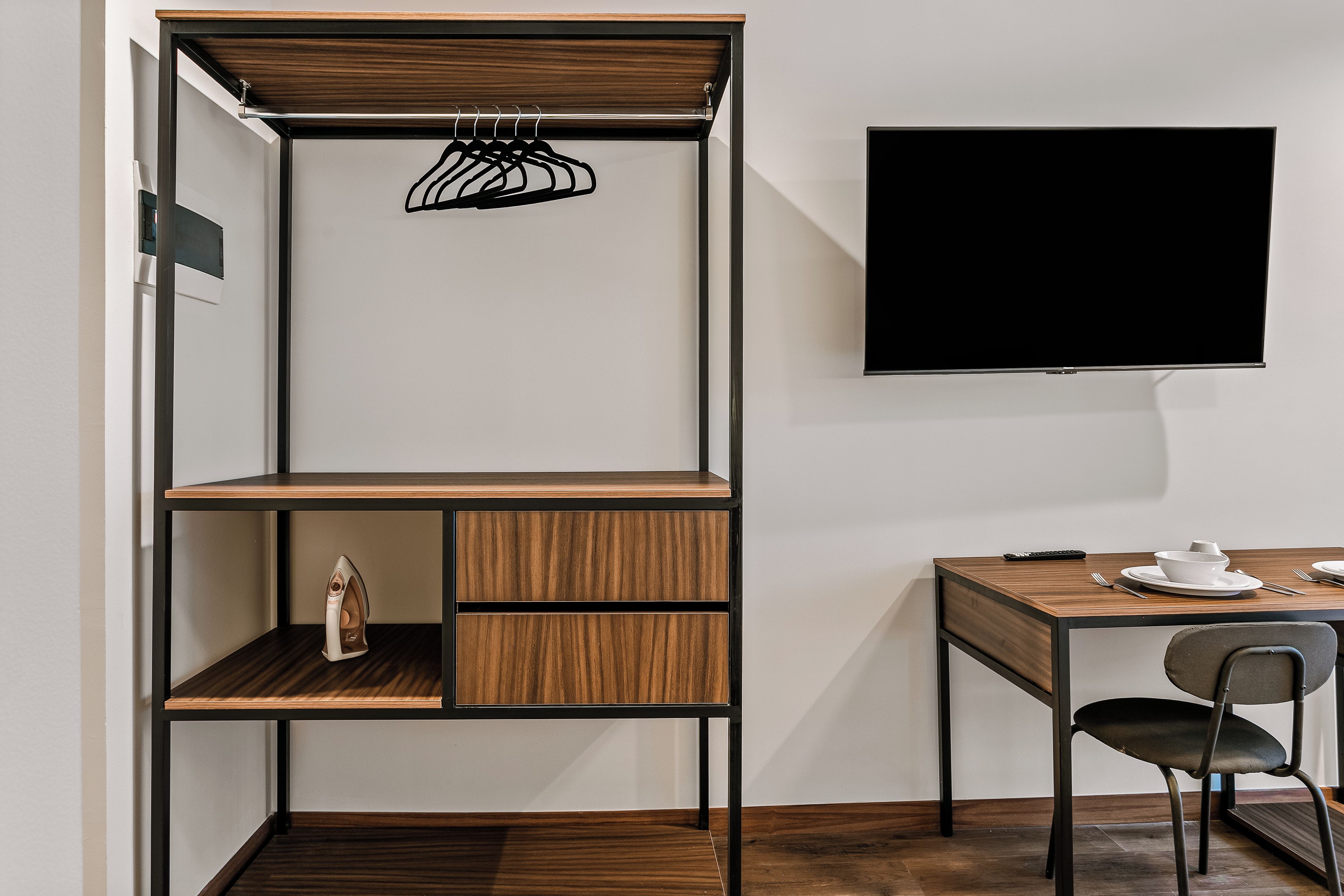 A modern room with a wooden desk, a chair, a flat-screen TV, and a built-in shelving unit with a hanging rack.