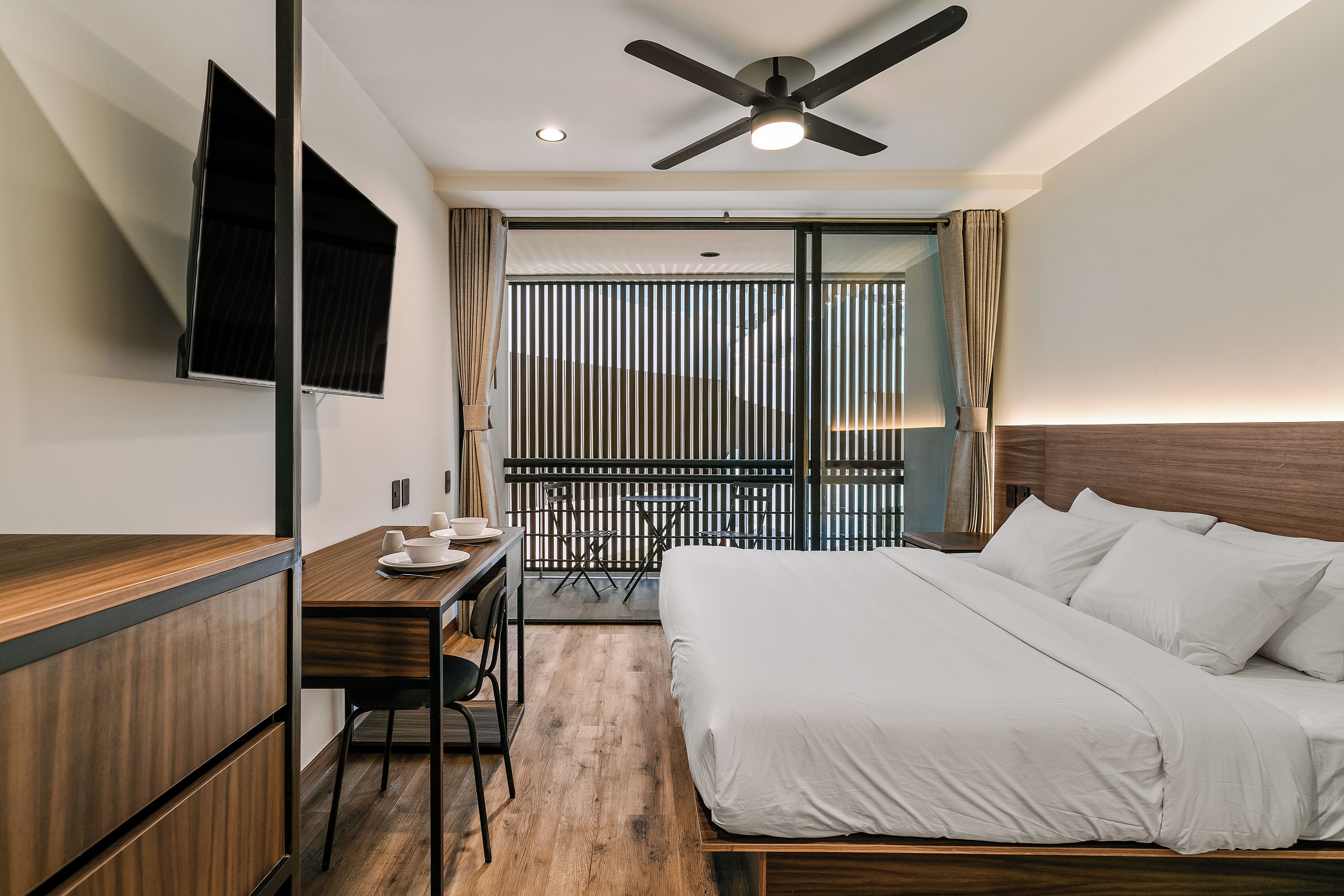 A hotel room with a bed, a desk, a chair, a TV, and a balcony with a view.