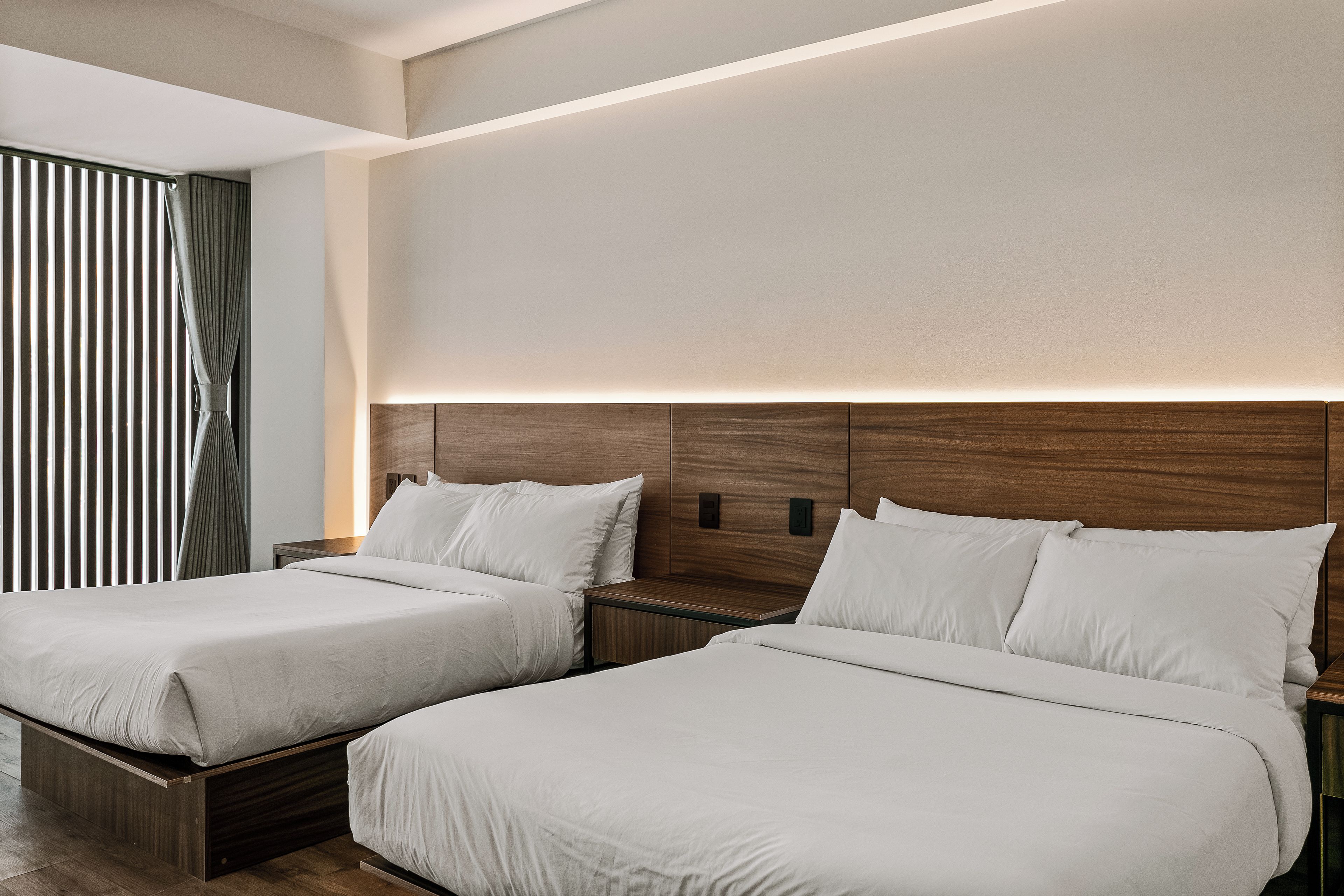 Una habitación de hotel con dos camas, un cabecero de madera y una mesita de noche con lámpara.