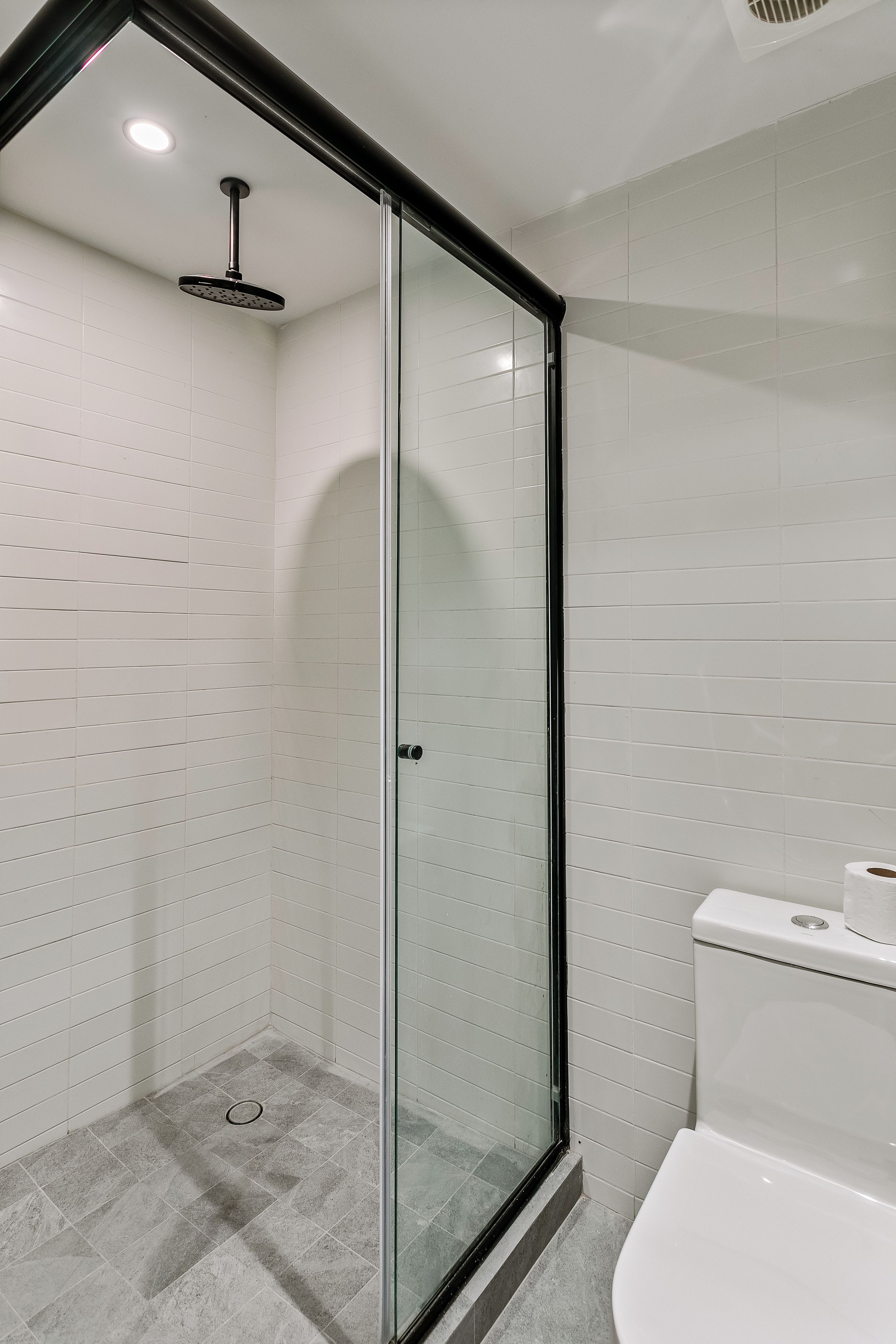 Un bagno moderno con cabina doccia in vetro, pareti piastrellate di bianco e un water bianco.