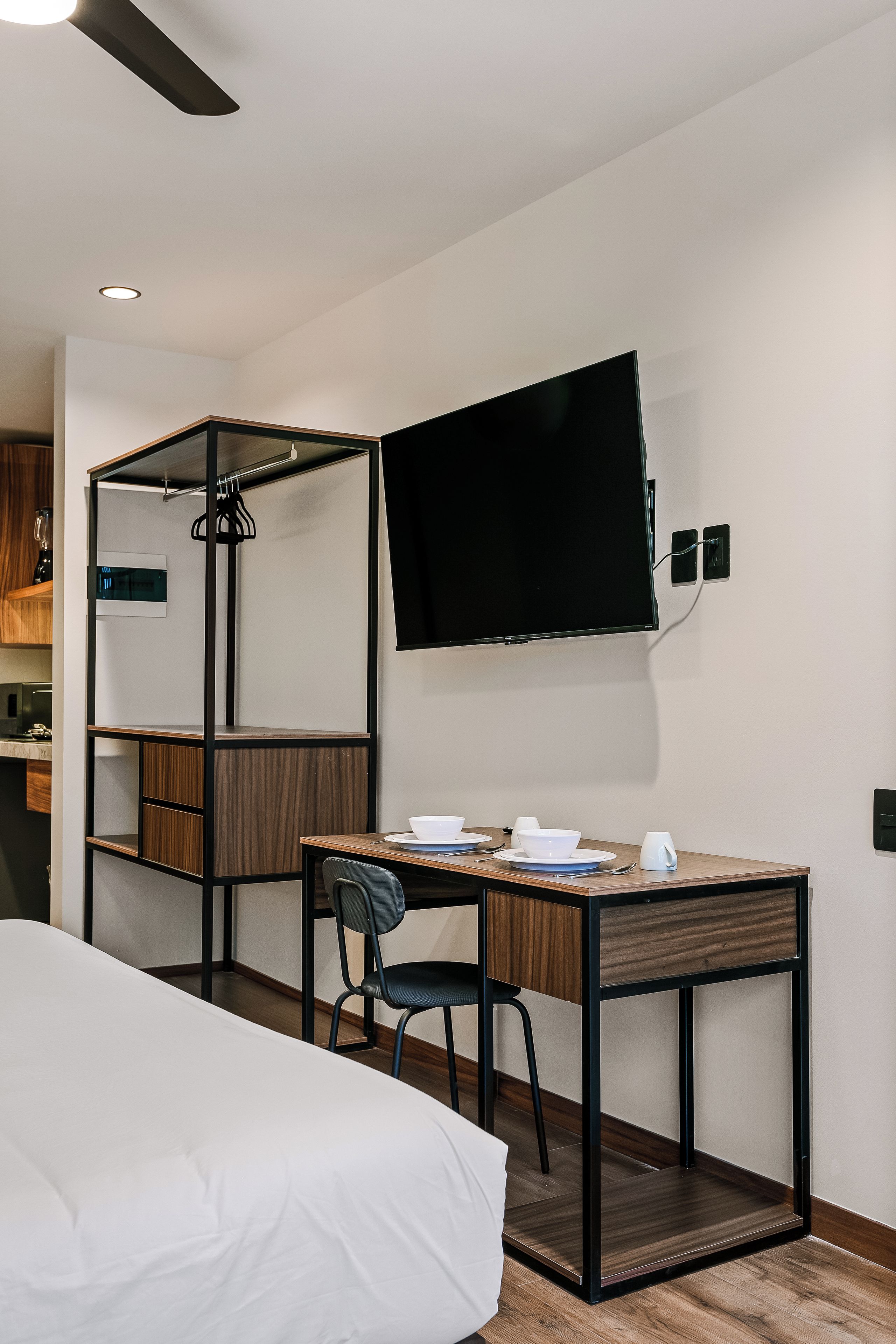 Une chambre d’hôtel comprenant un lit, un bureau avec une chaise, un téléviseur fixé au mur et une armoire avec un miroir.