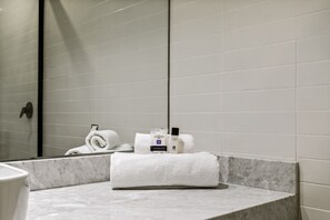 A bathroom with white tiles, a marble countertop, and a mirror reflecting a towel and toiletries. - Suites Álamos by Homirent (Querétaro)