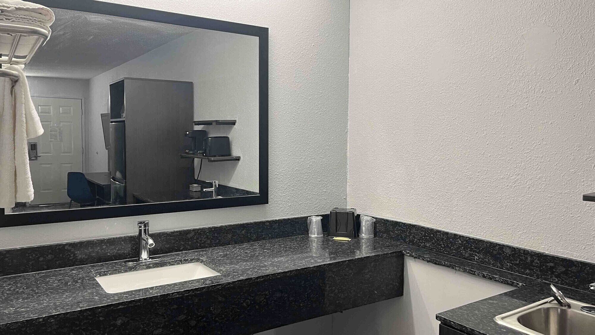 Ein modernes Badezimmer mit einem großen Spiegel, einem Waschbecken und einer Kaffeemaschine.