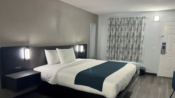 Une chambre d’hôtel moderne dotée d’un grand lit, de tables de chevet, d’une tête de lit avec éclairage intégré, d’un rideau à motifs et d’une porte équipée d’un système de verrouillage à carte magnétique.