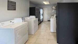 Une buanderie équipée de machines à laver et de sèche-linge Whirlpool, d’un réfrigérateur et d’un distributeur automatique.