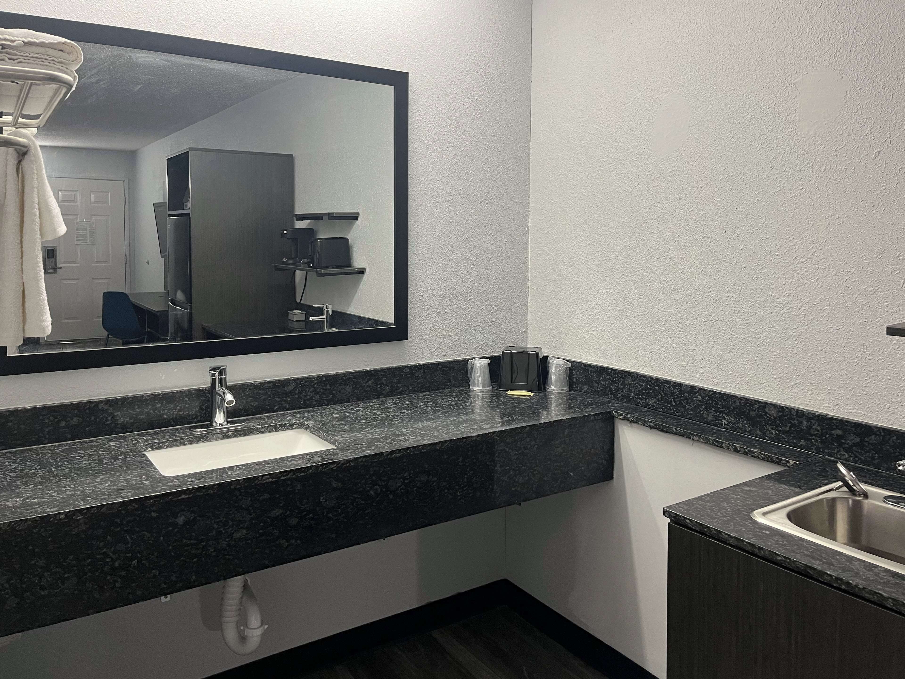 Un baño moderno con encimera de granito, lavamanos y un espejo grande.