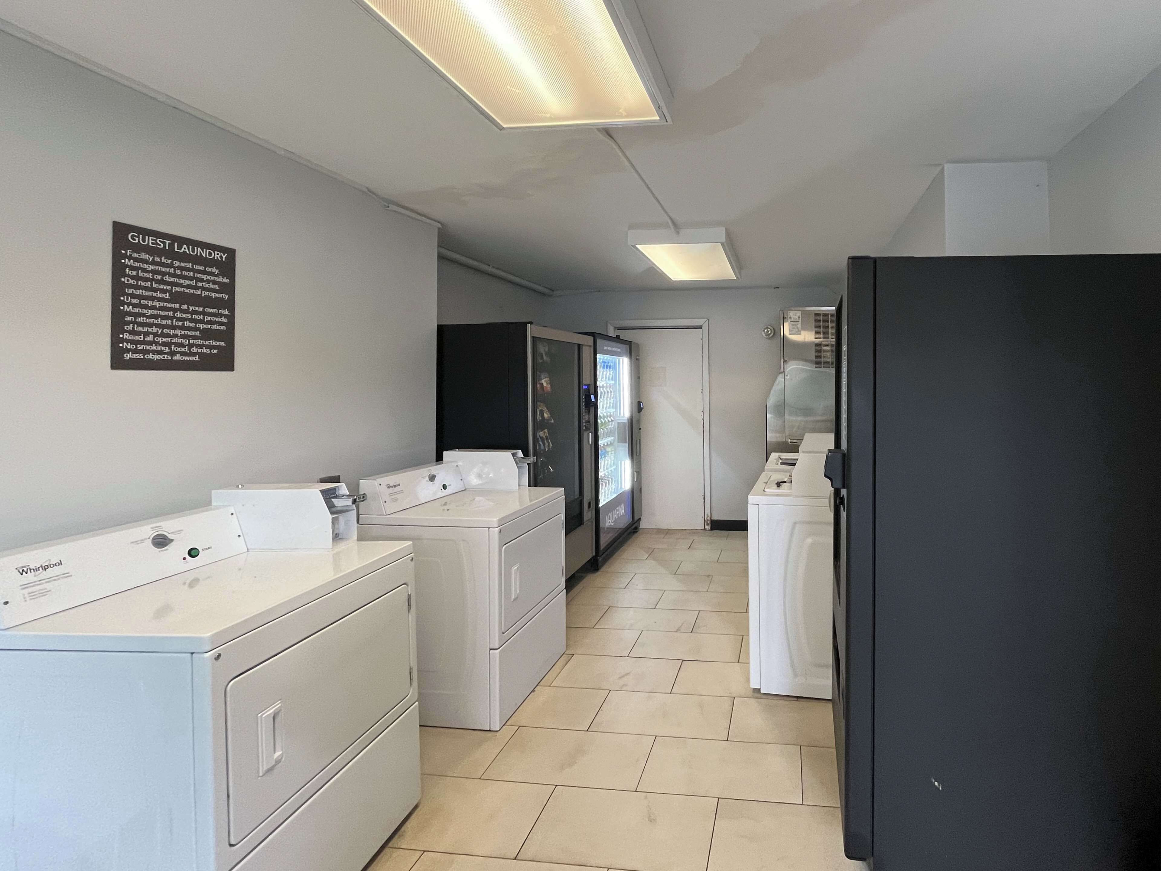 Een wasserette met Whirlpool wasmachines en drogers, een automaat en een bord met de regels voor het gebruik van de wasruimte door gasten.