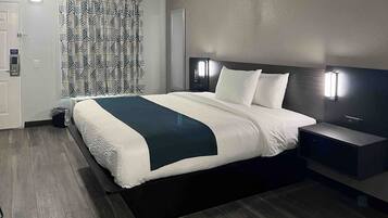 A modern hotel room with a large bed, a bedside table, and a headboard with integrated lighting.