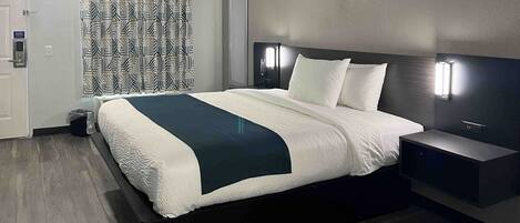 A modern hotel room with a large bed, a bedside table, and a headboard with integrated lighting.