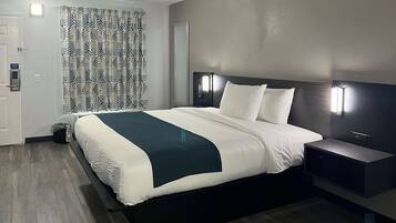 Een moderne hotelkamer met een groot bed, nachtkastjes, een hoofdbord met ingebouwde verlichting, een kamerbreed gordijn en een houten vloer.
