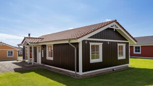 Een klein, gelijkvloers houten huis met een puntdak, witte details en een veranda.
