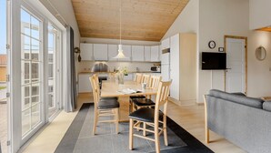 Een moderne keuken met witte kastjes, een houten plafond en een eethoek met een tafel en stoelen.