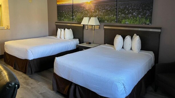 Habitación de hotel con dos camas, una mesita de noche, una lámpara y un cuadro grande de un campo al atardecer.