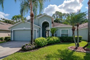 A single-story house with a garage, surrounded by a well-maintained lawn and palm trees.