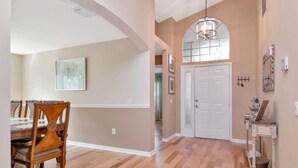 A hallway with wooden flooring, a dining area with a wooden table and chairs, and a white door. - Deer Run in Wesley Chapel 4br-3ba (Zephyrhills)