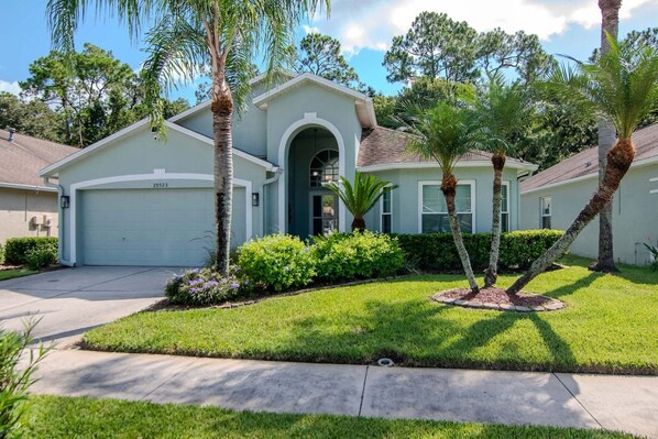A residential house with a garage, a well-maintained lawn, and palm trees.