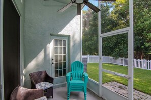 A covered porch with wicker chairs, a door, and a view of a white fence and green lawn. - Deer Run in Wesley Chapel 4br-3ba (Zephyrhills)