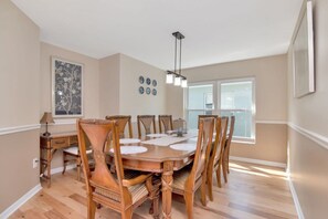 A dining room with a wooden table and chairs, a chandelier, a window, and wall decorations.