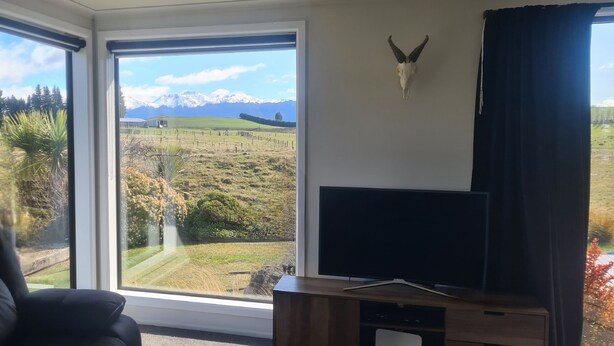 A room with a large window offering a view of a mountainous landscape, a mounted animal skull on the wall, and a television on a wooden stand.