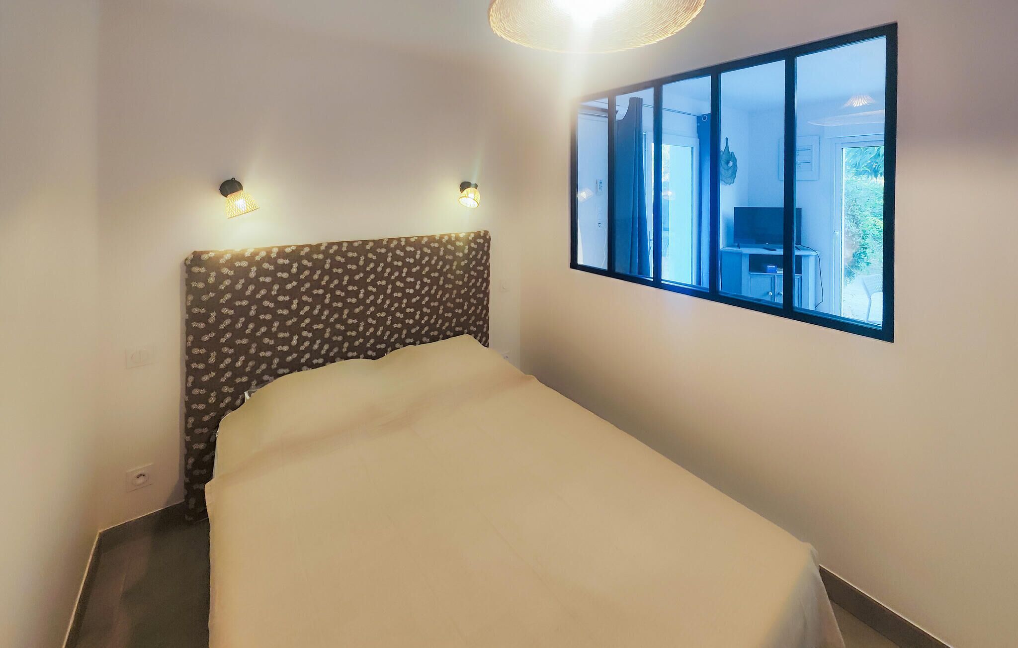 A bedroom with a bed, a patterned headboard, two wall-mounted lights, and a window with a view of the outdoors.
