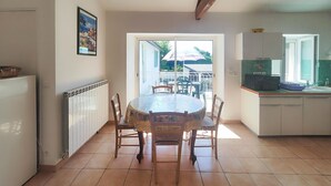 Una cocina con una mesa redonda y sillas, un refrigerador, un microondas y una ventana con vista a un jardín.
