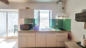 Cocina compacta con microondas, pileta y salpicadero de azulejos verdes.