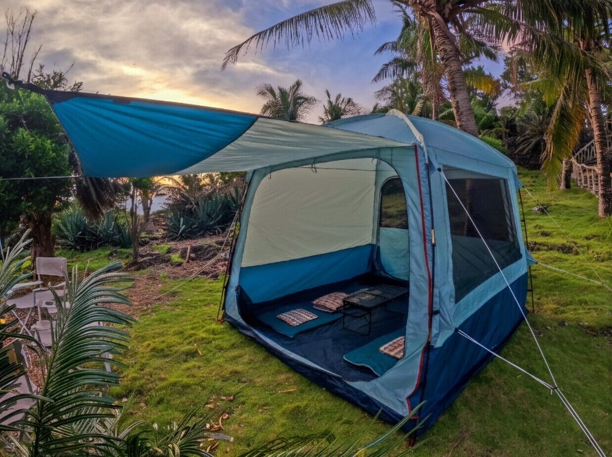 Een blauwe tent met een luifel, op een gazon met palmbomen op de achtergrond.