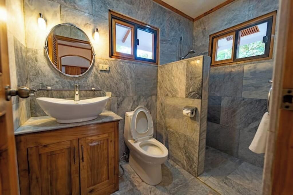 Ein Badezimmer mit Marmorbecken, Holzschränken, Toilette und Duschbereich.