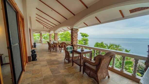Un espace extérieur abrité, avec vue sur la mer, aménagé avec des chaises et des tables en osier, et doté d’un sol carrelé.