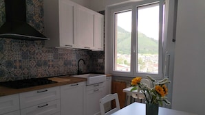A kitchen with white cabinets, a black range hood, a tiled backsplash, a window with a view of a town, and a table with a vase of flowers. - Family apartment near Salerno, the Amalfi and Cilento coasts. (Baronissi)