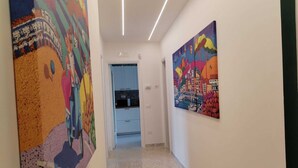 A hallway with colorful abstract paintings on the walls, a kitchen area with light blue cabinets, and a tiled floor. - Family apartment near Salerno, the Amalfi and Cilento coasts. (Baronissi)